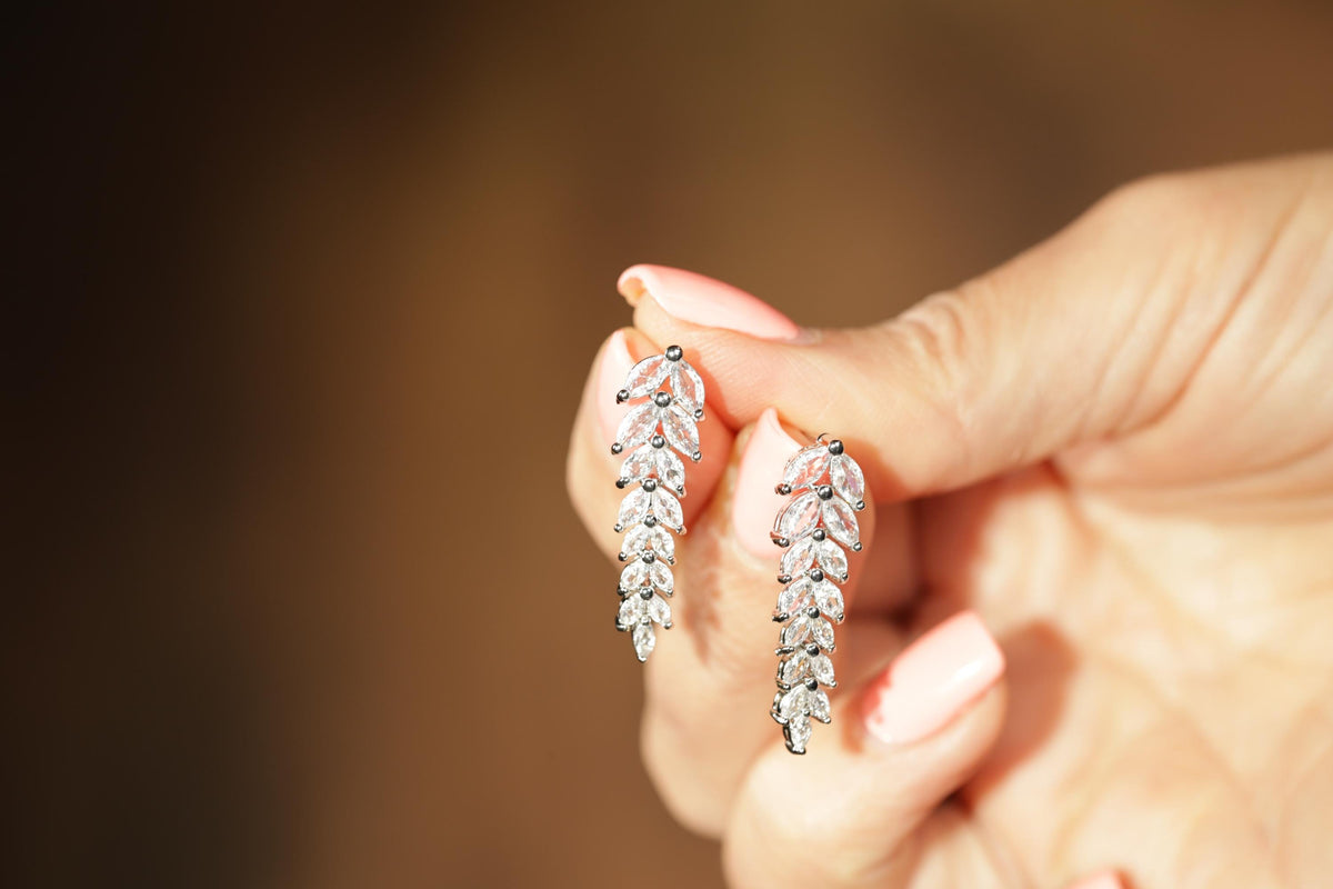A hand holding a pair of silver earrings with leaf-shaped designs.