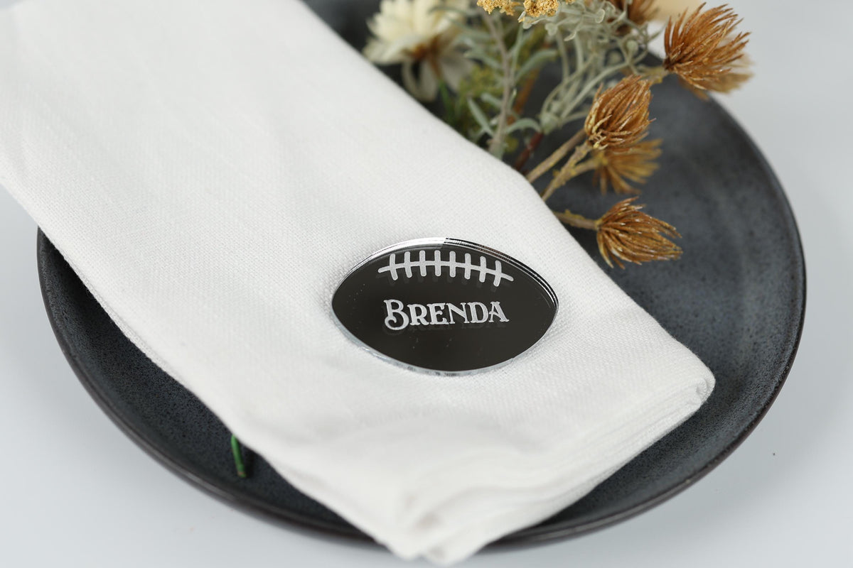 A white napkin with a black oval-shaped nameplate on it, placed on a black plate.