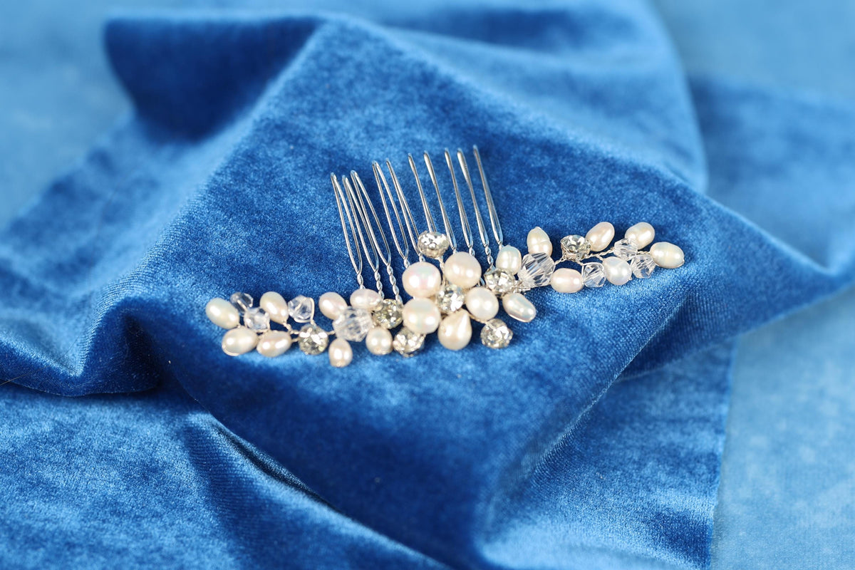 A silver hairbrush with white pearls and crystals rests on a blue velvet background.