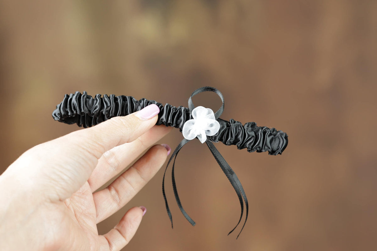 A hand holding a black garter belt with a white flower on it.