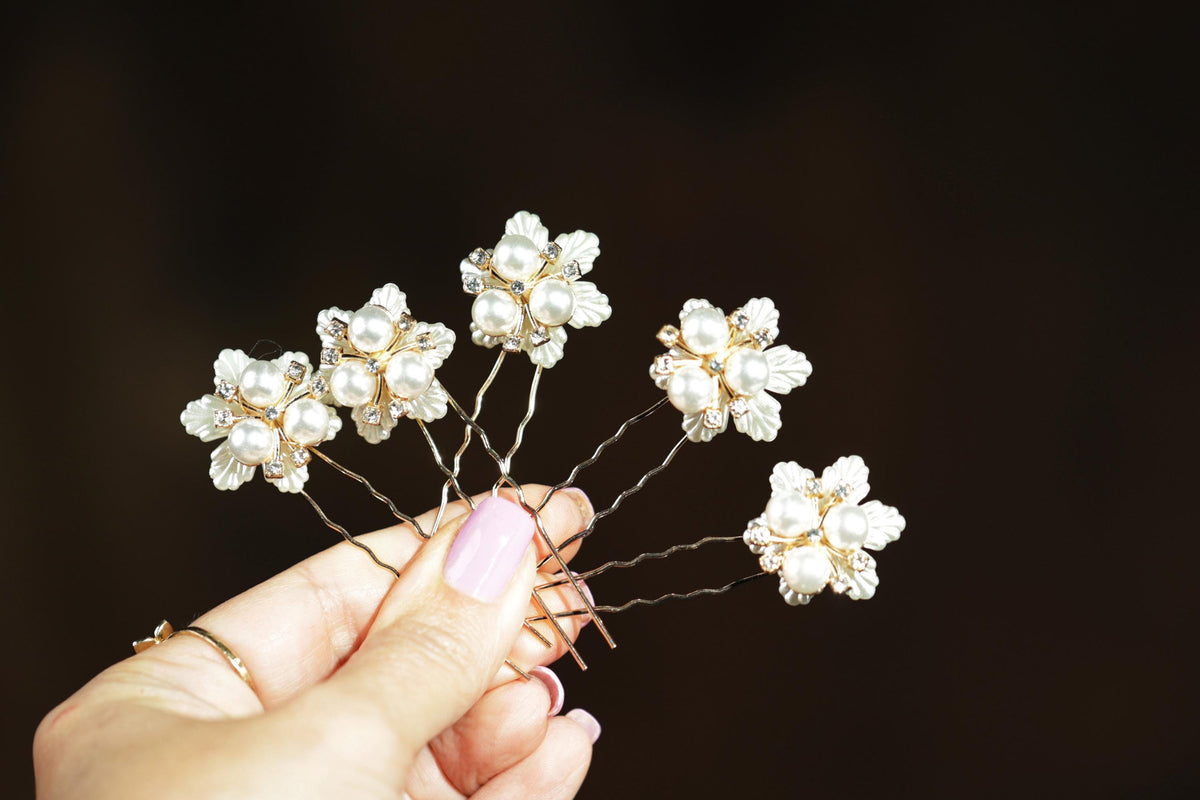 A hand holding a set of decorative hair clips with white flowers on them.