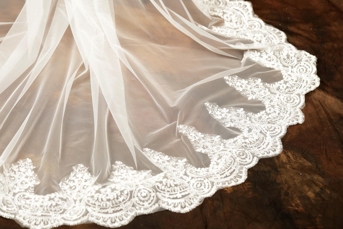 A close-up view of a delicate white wedding veil with intricate lace trim, resting on a wooden surface.