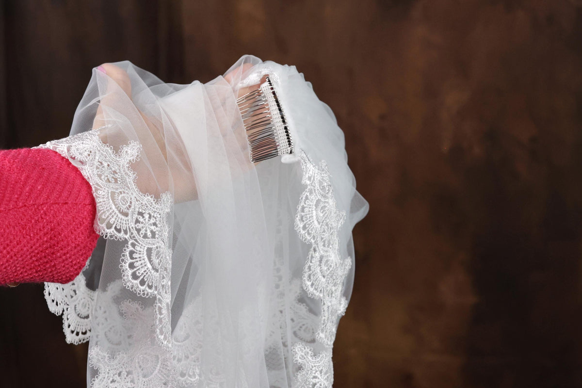 A hand holding a white veil with a metal comb attached to it.