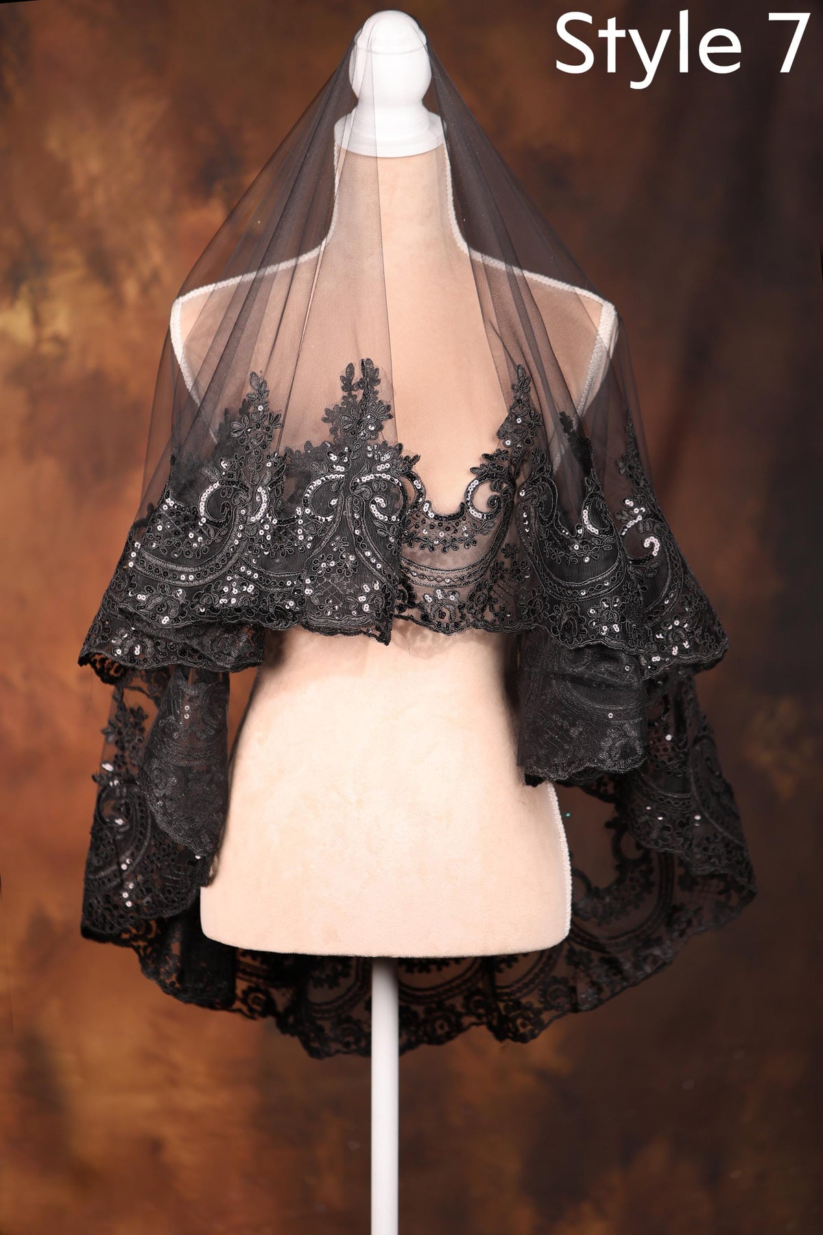 A mannequin wearing a black lace veil with intricate floral patterns, displayed against a brown background.