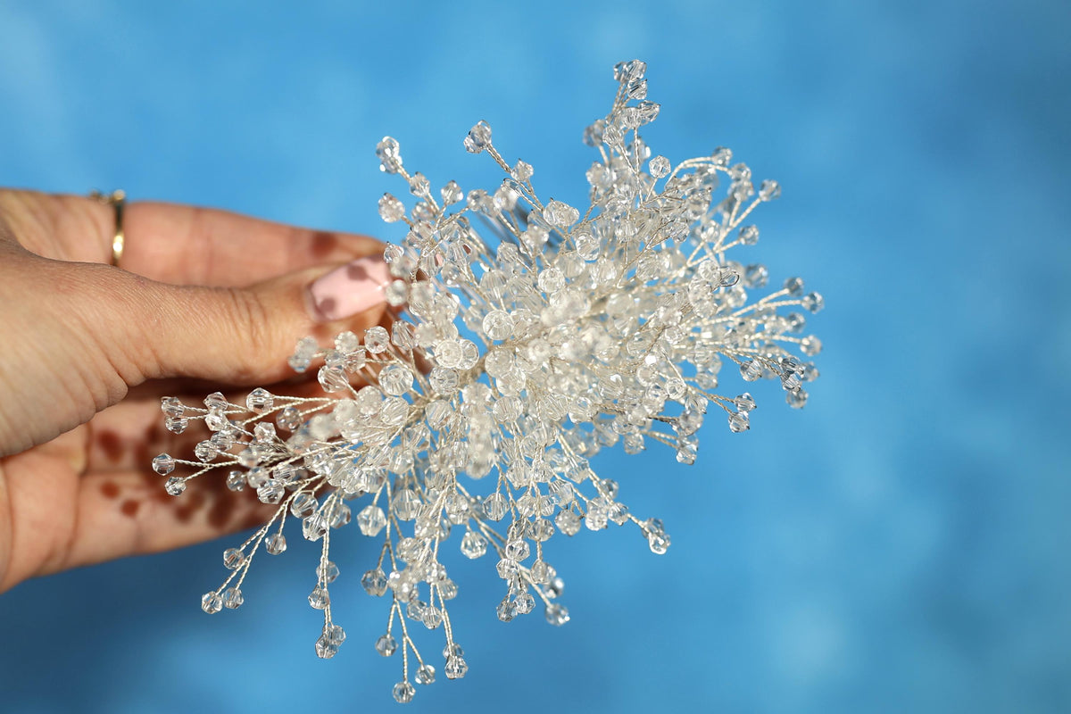 A hand holding a delicate, crystal-like flower against a bright blue background.
