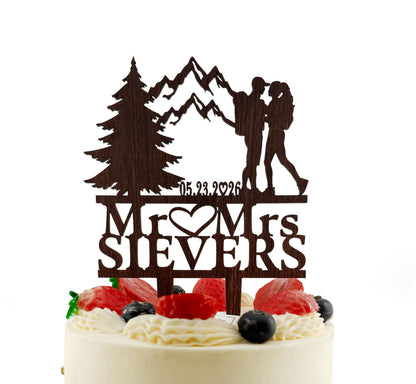 A cake topper with a silhouette of a couple and mountains, along with the text "Mr. & Mrs. Siever's" and the date "05.23.2026".