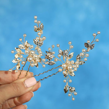 A hand holding a decorative hair clip with small pearls and leaves on a blue background.