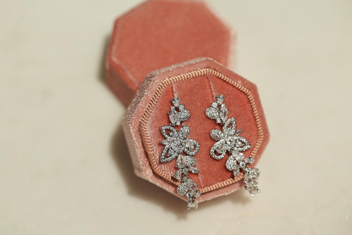 A pair of elegant diamond earrings rests in a pink velvet box, showcasing their intricate design and sparkling gemstones.