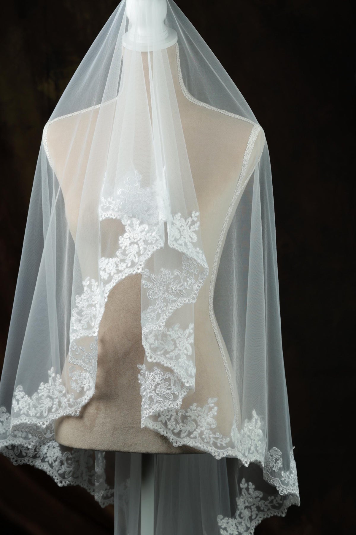 A mannequin wearing a white veil with intricate lace detailing.