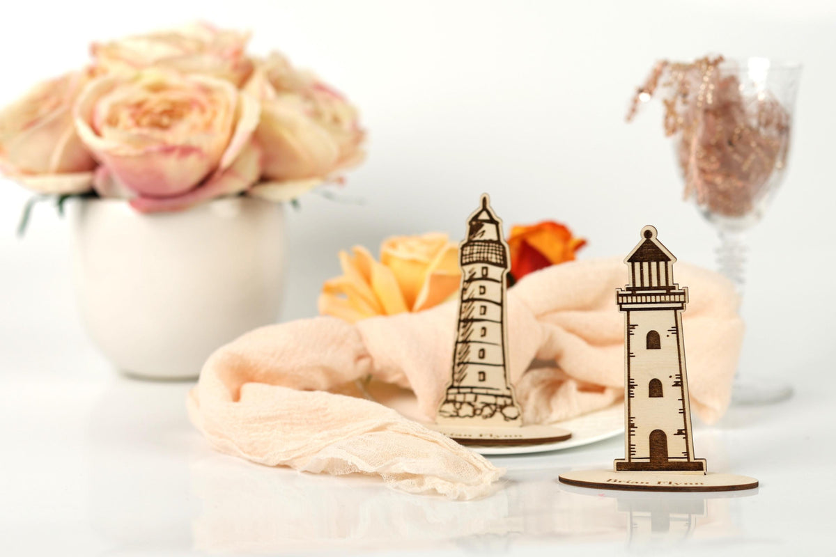 a white vase with pink roses, a wooden lighthouse, and a glass vase with a pink flower, all arranged on a white surface.