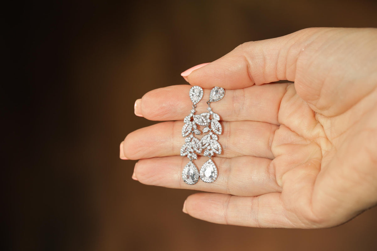A hand holding a pair of diamond earrings against a blurred background.