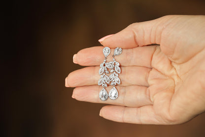 A hand holding a pair of diamond earrings against a blurred background.