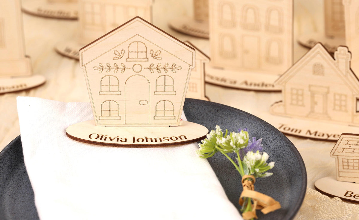 a wooden house-shaped place card holder with a nameplate, placed on a table with a plate of flowers and a small bouquet.