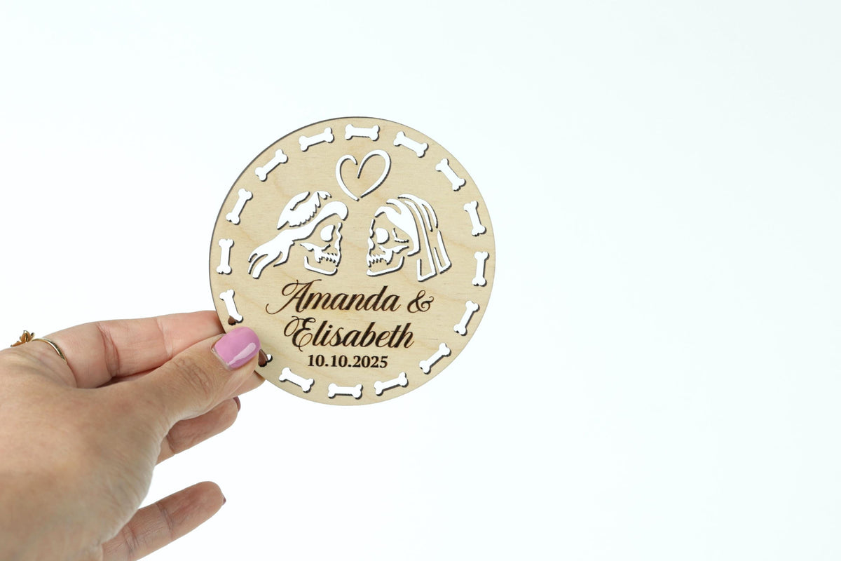 A hand holding a wooden coaster with a design featuring two people and a heart.