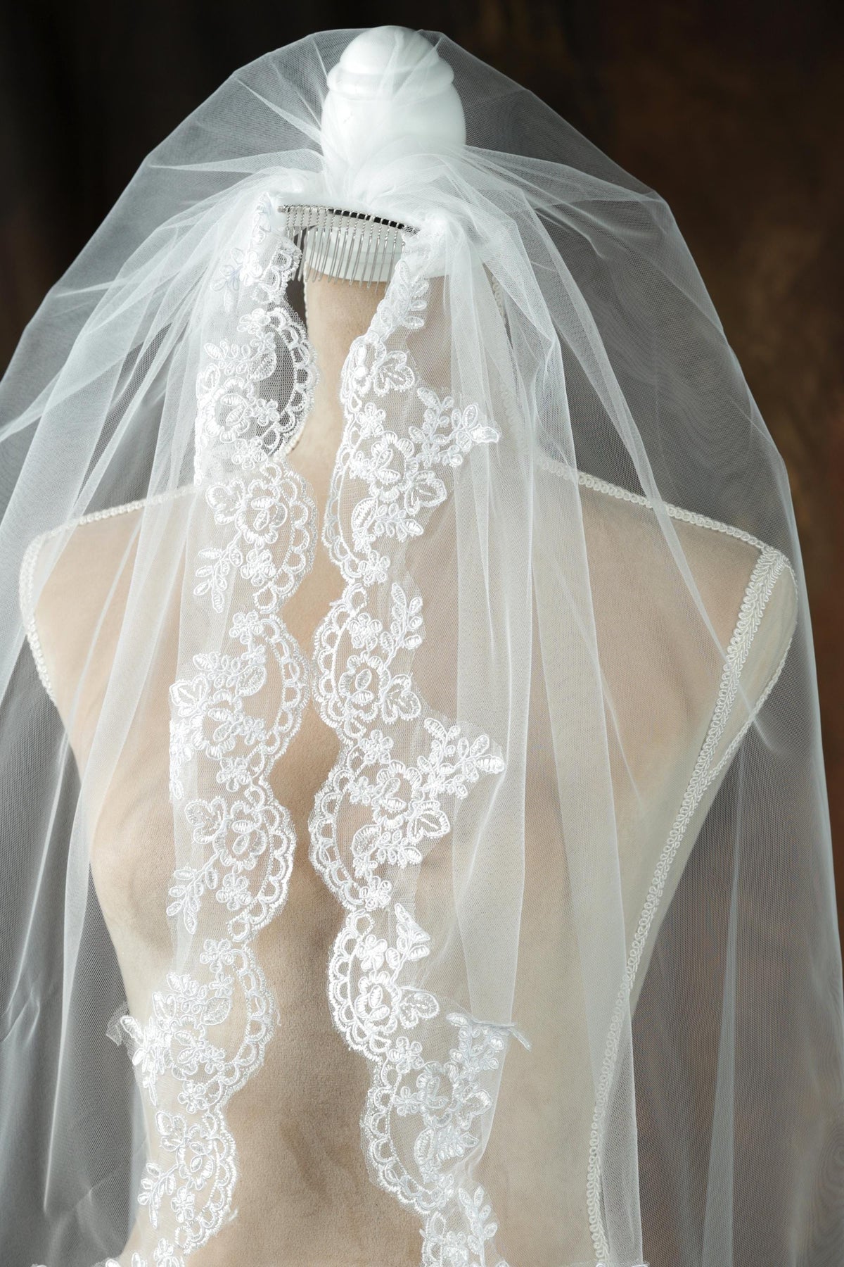 A mannequin wearing a white wedding veil with intricate lace detailing.