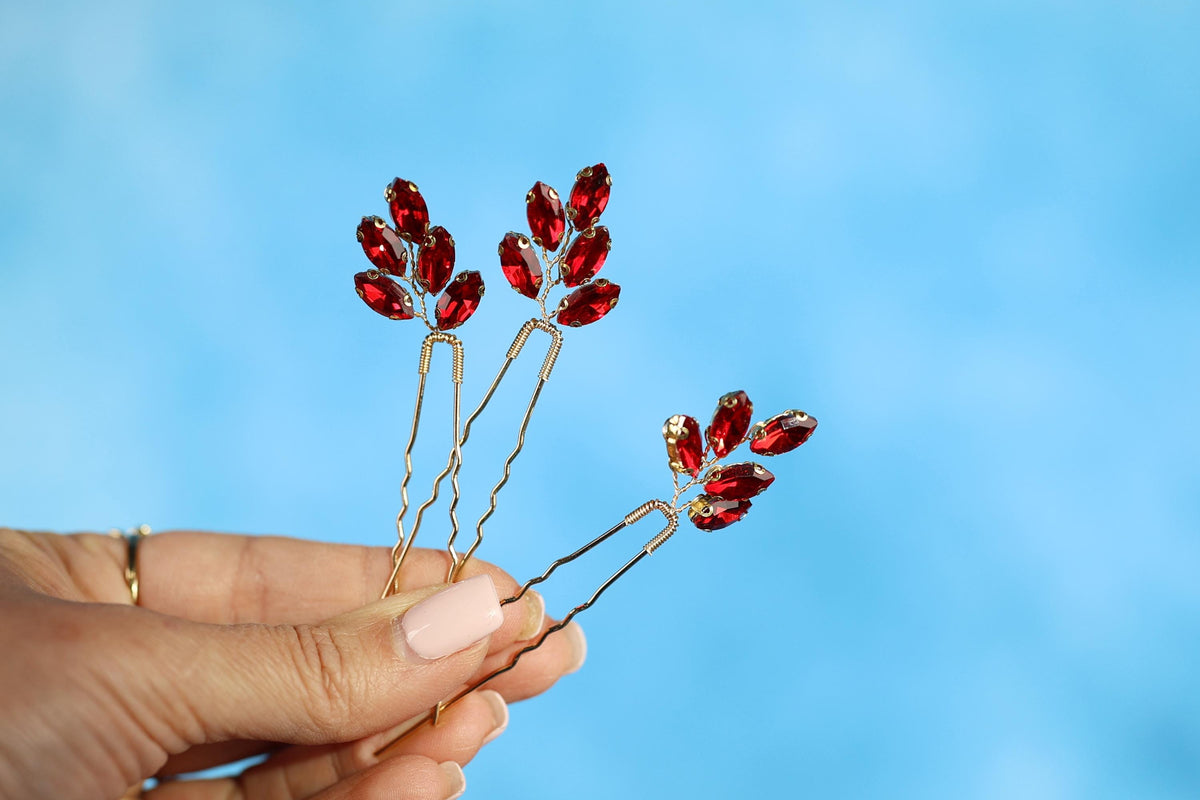 A hand holding three red gemstone hair clips against a blue background.