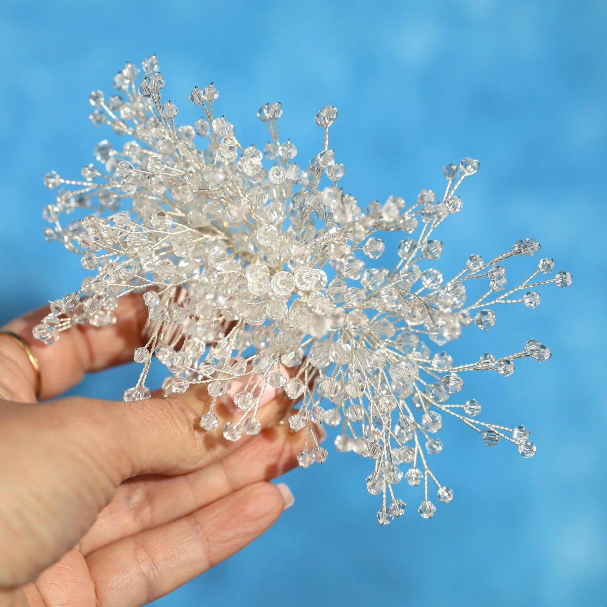 A hand holding a cluster of small, clear crystal branches against a blue background.