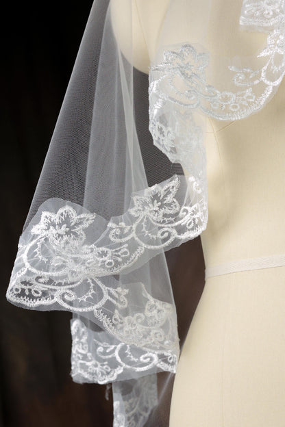 A close-up view of a delicate white lace veil with intricate floral embroidery, displayed on a mannequin.