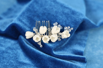 A white flower hair accessory with clear crystals is placed on a blue velvet background.