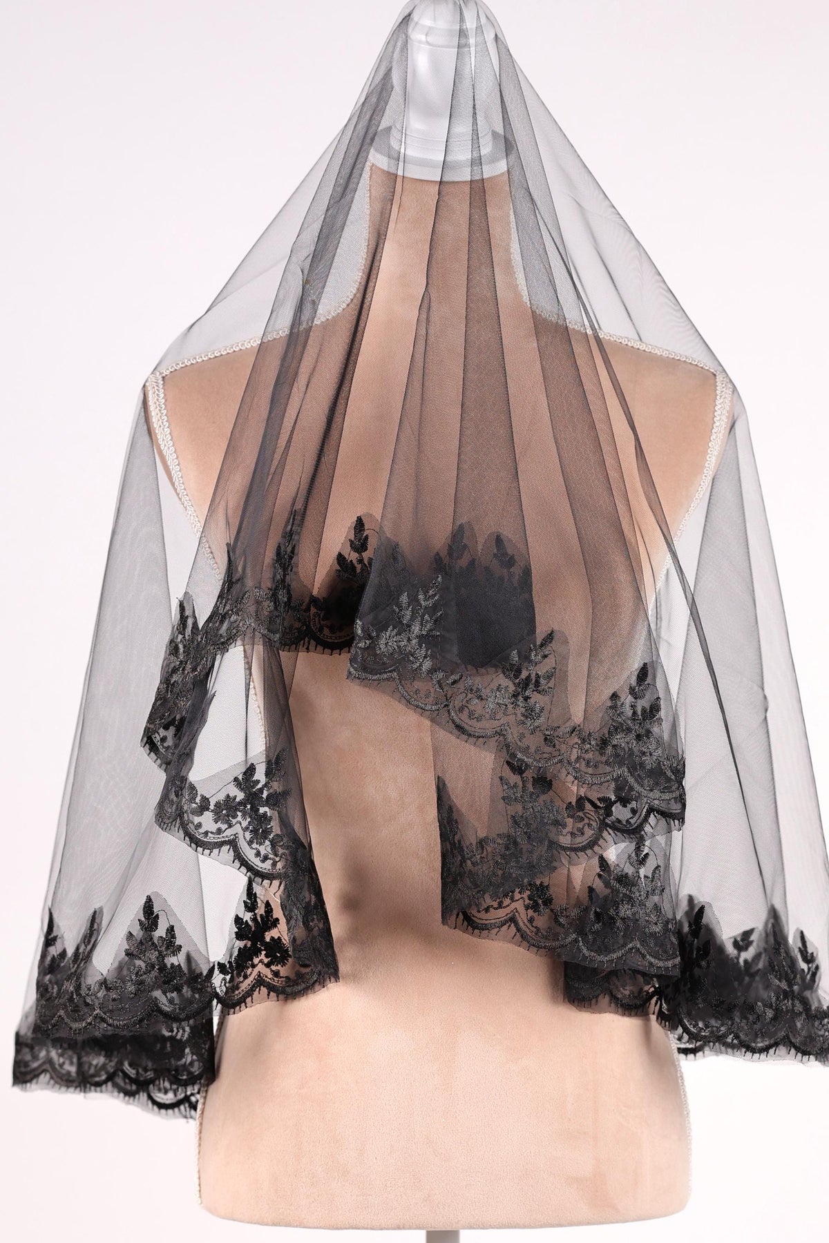 A mannequin wearing a black lace veil with intricate floral patterns.