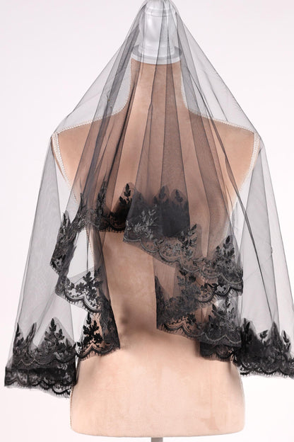 A mannequin wearing a black lace veil with intricate floral patterns.