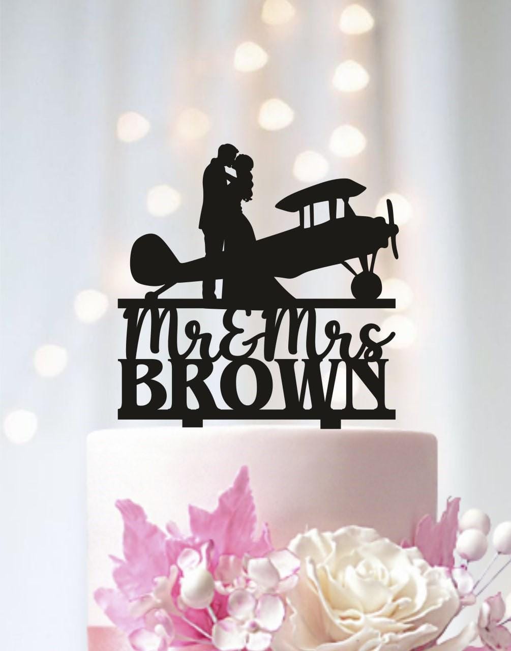 A black silhouette of a couple embracing an airplane on a cake topper, with the text "Mr & Mrs Brown" below it.