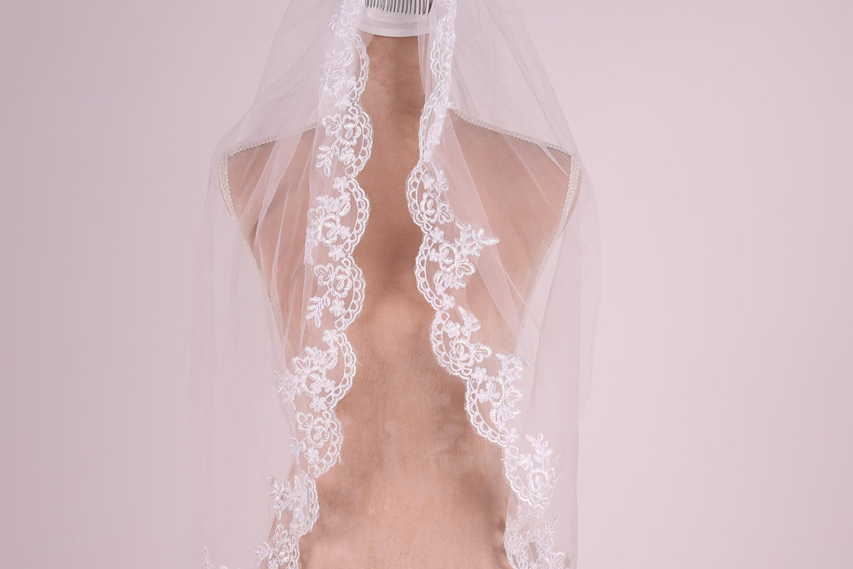 A mannequin wearing a white lace wedding veil with intricate floral embroidery.