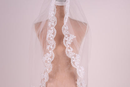 A mannequin wearing a white lace wedding veil with intricate floral embroidery.