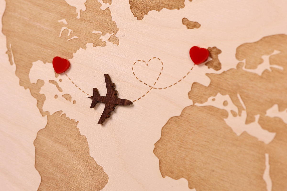 A wooden world map with a small airplane and two red heart-shaped objects representing a couple or loved ones, symbolizing travel and love.