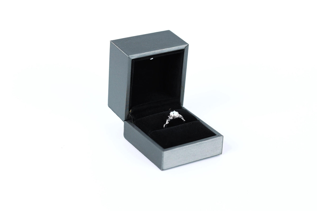 A silver engagement ring is displayed in a black jewelry box against a white background.