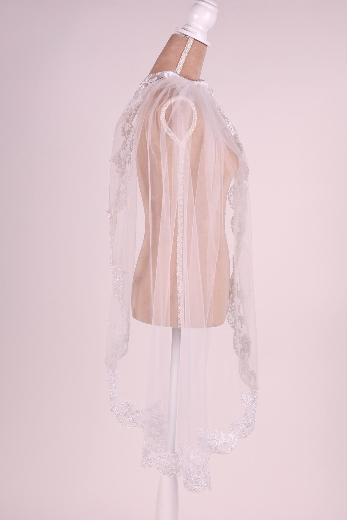 A white mannequin wearing a white lace veil with a delicate floral pattern.