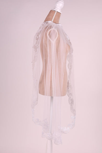 A white mannequin wearing a white lace veil with a delicate floral pattern.