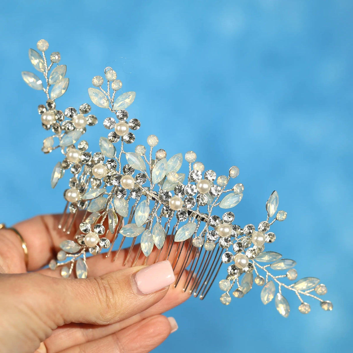 A hand holding a decorative hair accessory with small white and clear gemstones.