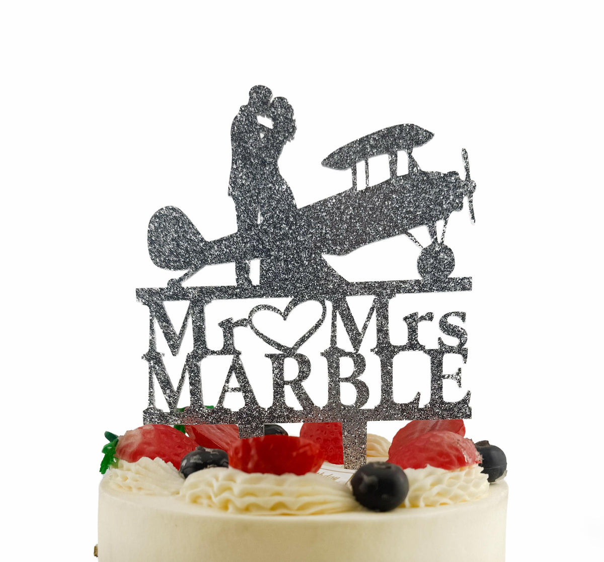 A wedding cake with a decorative topper featuring a silhouette of a couple embracing, along with the text "Mr. Marble" and an airplane silhouette.