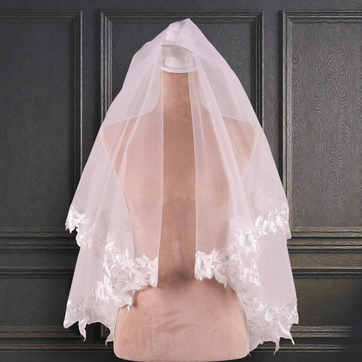 A white wedding veil with delicate lace trim is displayed on a mannequin head against a dark background.