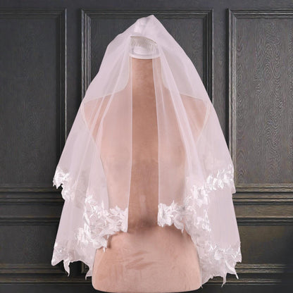 A white wedding veil with delicate lace trim is displayed on a mannequin head against a dark background.