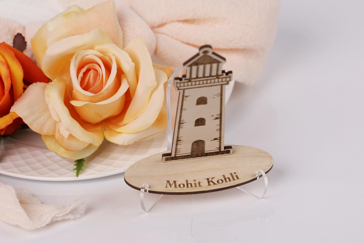 a wooden lighthouse model placed on a white surface, with a large orange rose and a white towel in the background.
