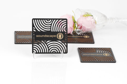 a business card stand with a black and white striped design, a glass of wine with a pink rose, and some coasters with the word "Soundscape" printed on them.