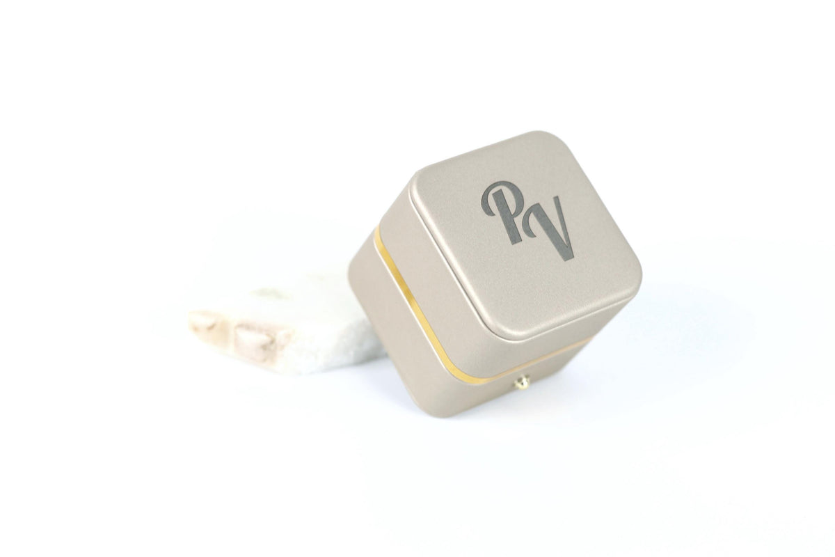 A square metal box with a logo on it, placed on a white surface.