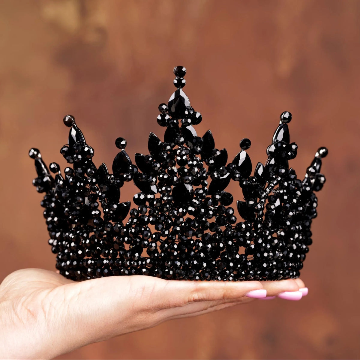 a hand holding a black crown made of beads