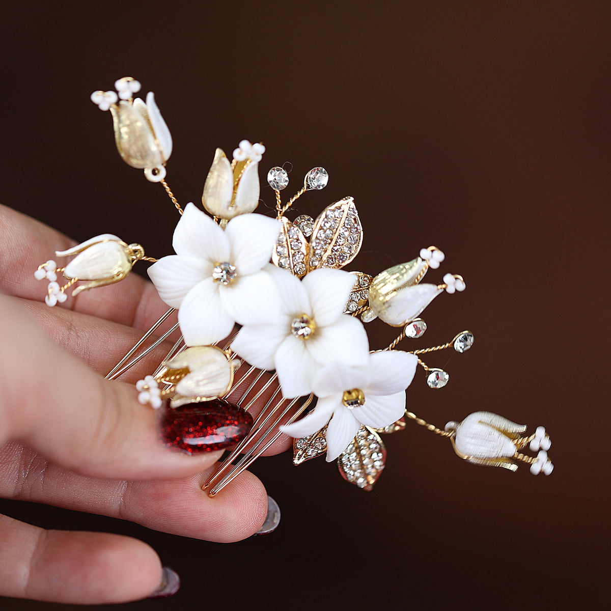 A hand holding a decorative hair accessory with white flowers and gold accents.