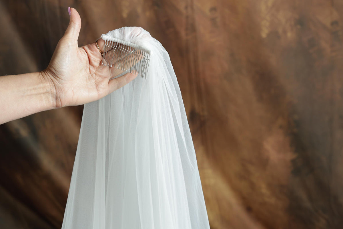 A hand holding a white veil against a brown background.