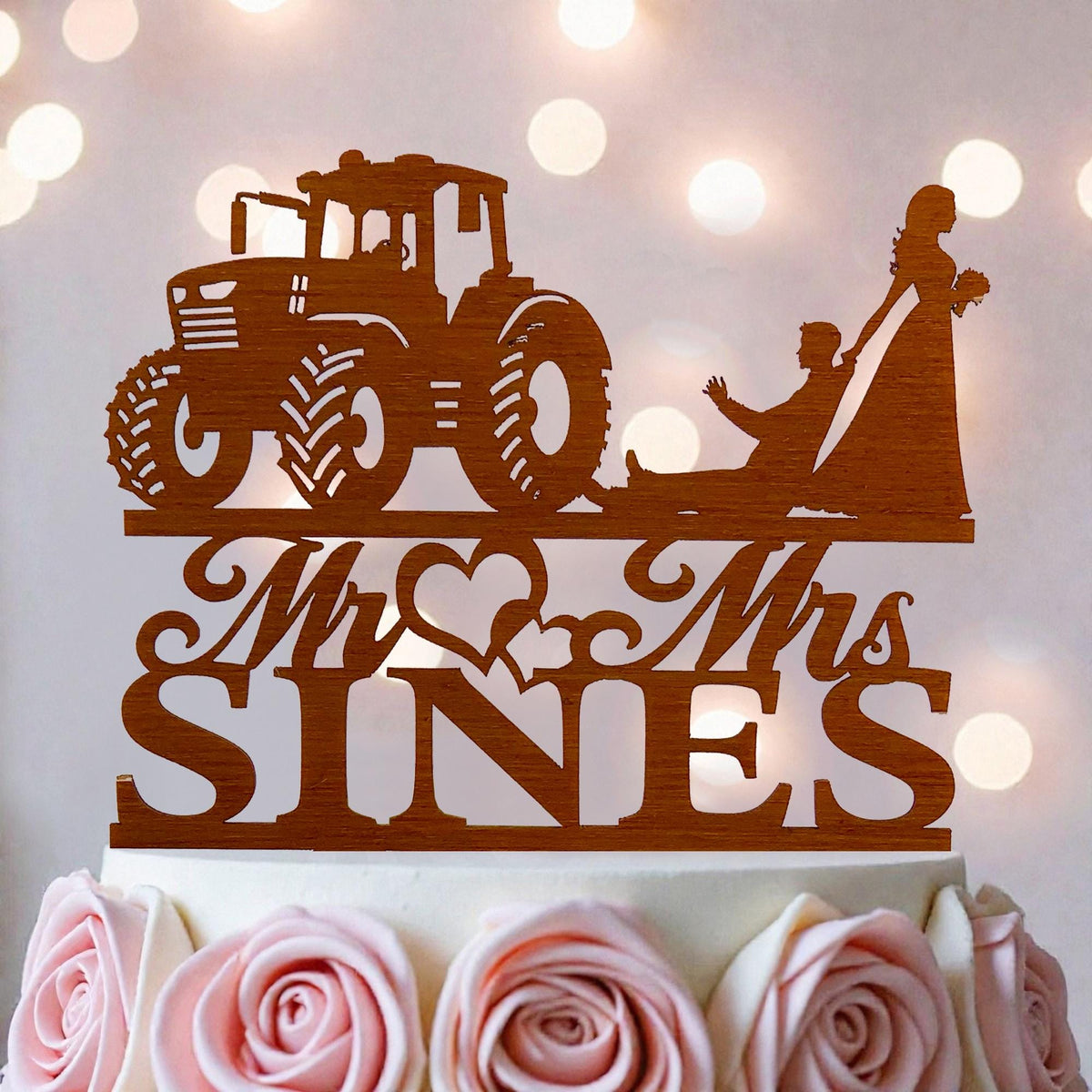 A wooden wedding cake topper with a tractor and a bride and groom silhouette.