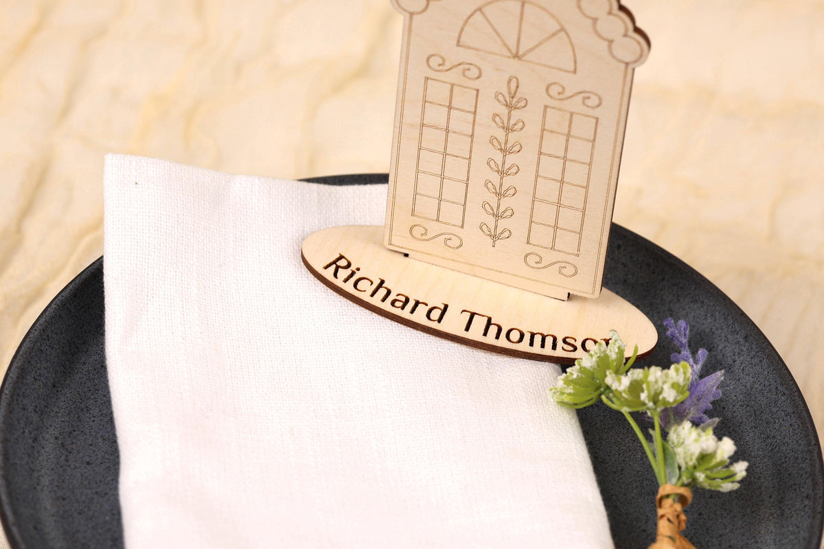 A wooden place card holder with a nameplate sits on a white napkin, accompanied by a small bouquet of flowers.