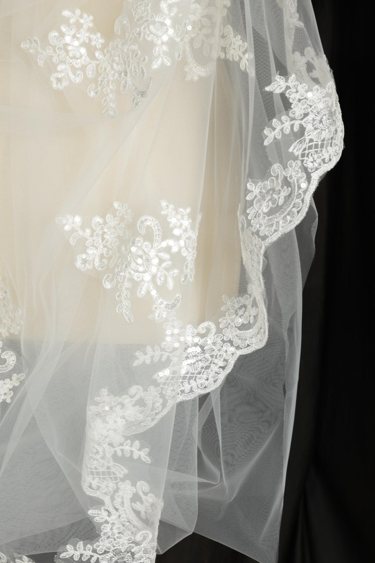A close-up view of a delicate white wedding veil with intricate lace and floral embroidery.