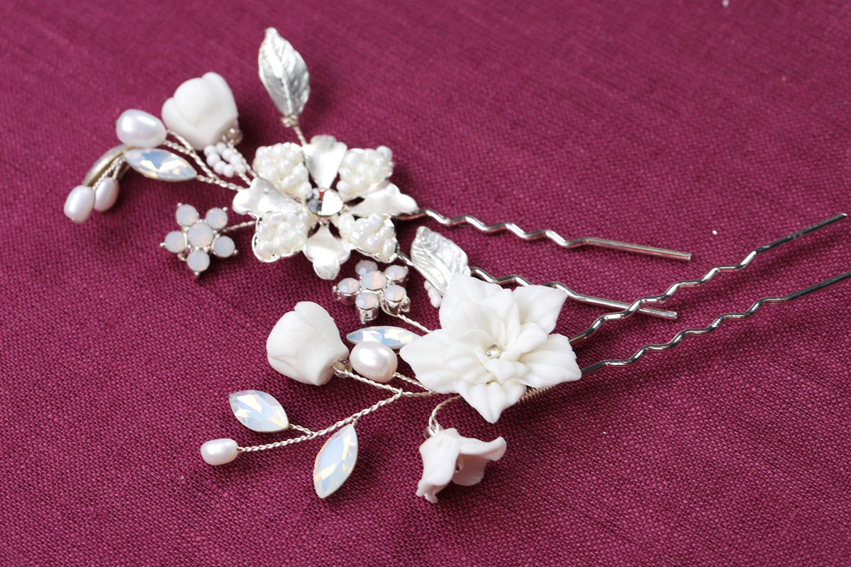 A close-up image of a decorative hair clip with white flowers and pearls on a red background.