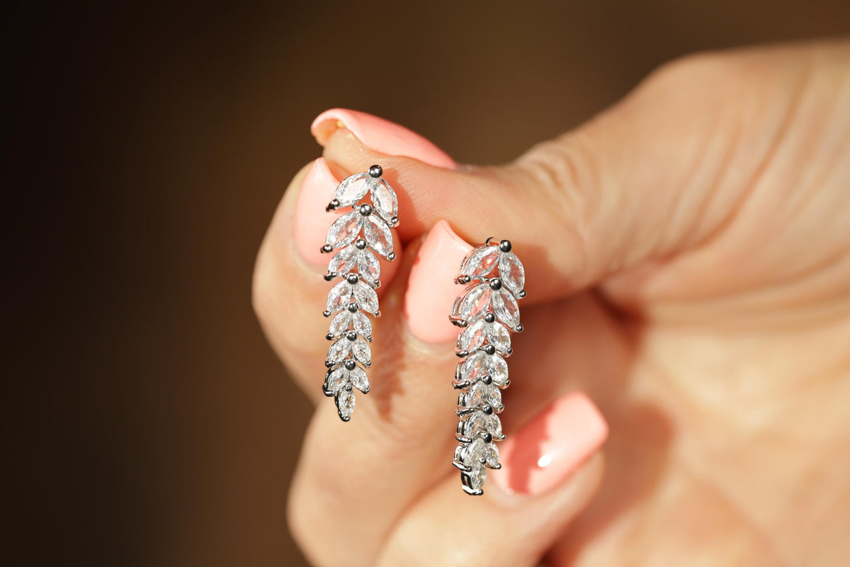 A close-up of a person's hand holding a pair of diamond earrings with a floral design.