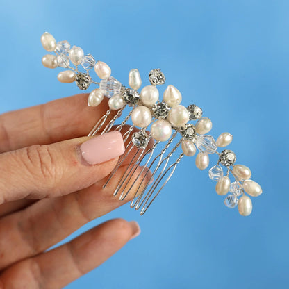 A hand holding a decorative hair accessory with pearls and crystals against a blue background.
