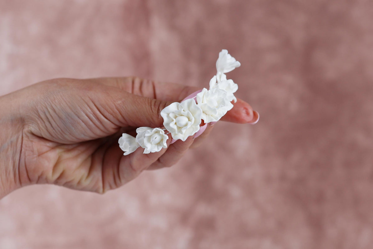 A hand holding a cluster of white flowers against a pink background.