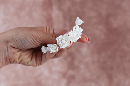 A hand holding a cluster of white flowers against a pink background.